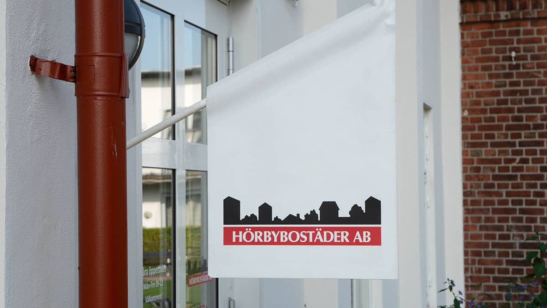 Liten vit flagga med Hörbybostäders logotyp hänger från en fasad.