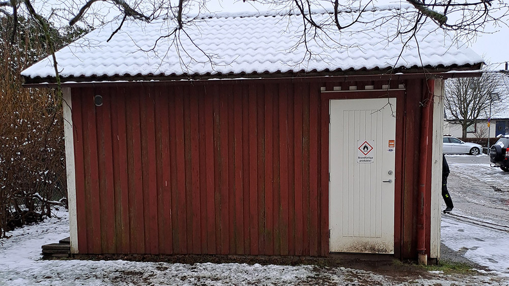 Sida av rödmålad förrådsbyggnad med enkeldörr.