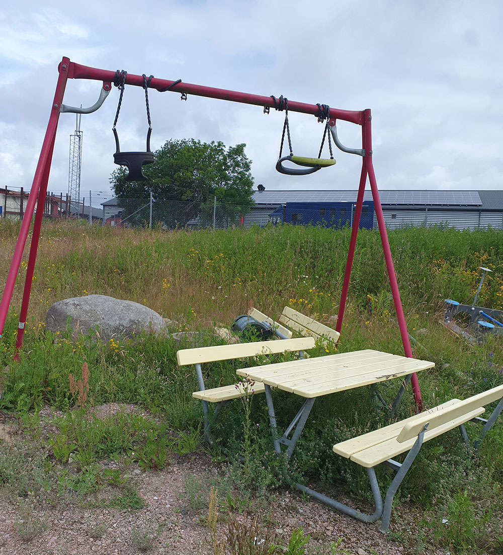 Röd barngungställning i högt gräs. Framförngställningen står en kombinera bänk/bord